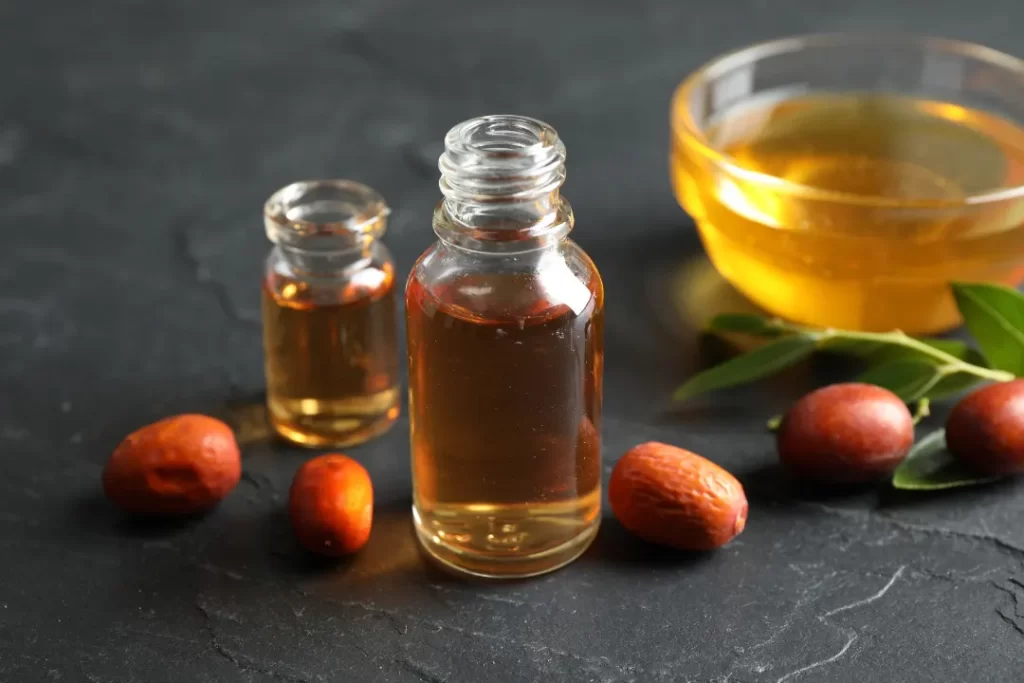 Jojoba Oil in Glass Bottle and Seeds on Light Grey Table