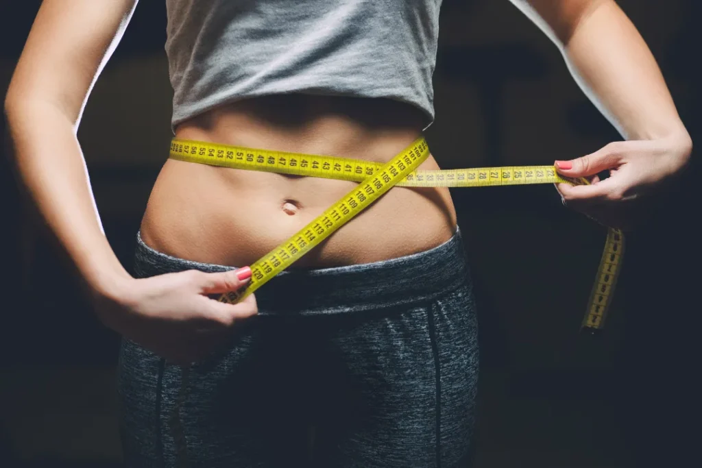 Young fit Girl holding an inch of tape around her waist. 