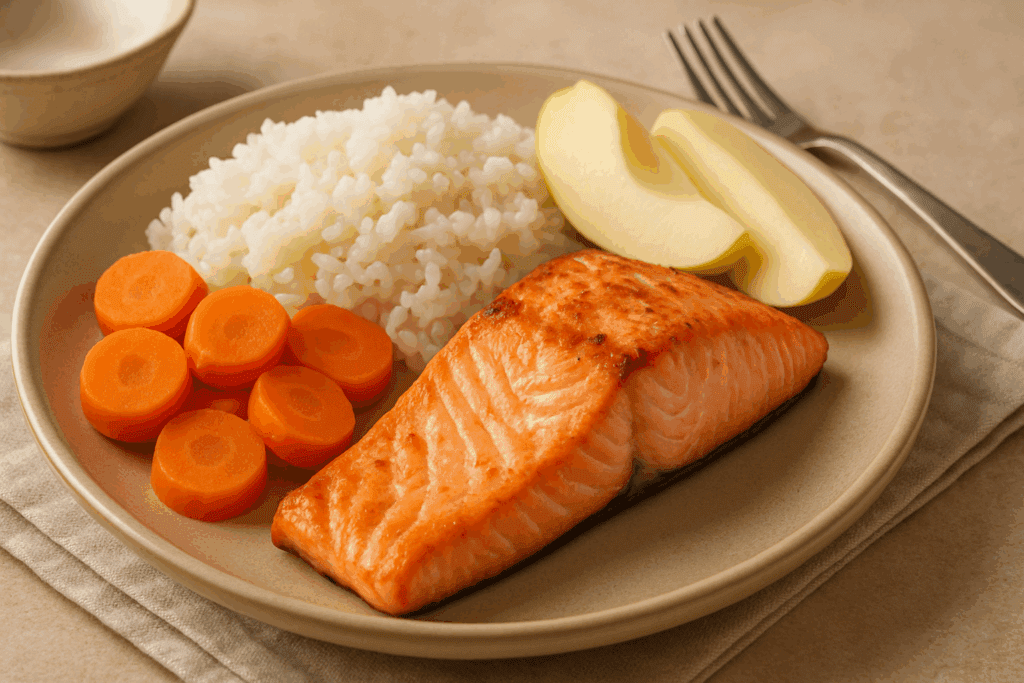 Grilled salmon, steamed carrots, white rice, and peeled apple slices on a beige plate, representing a gut-friendly ulcerative colitis diet.

